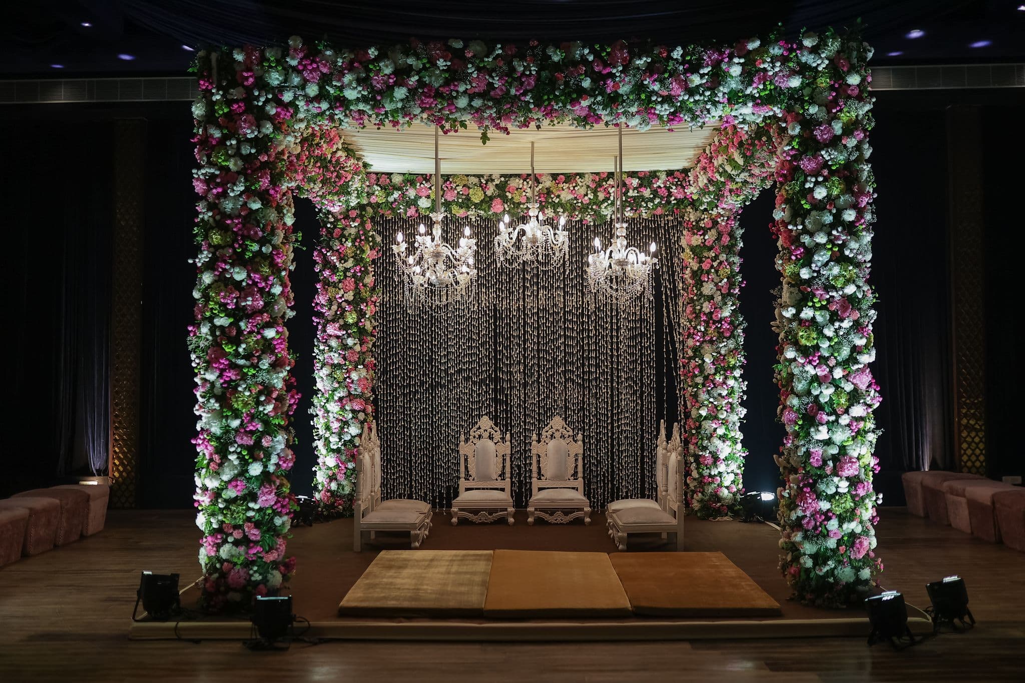 A wedding mandap dressed in flowers under crystal chandeliers
