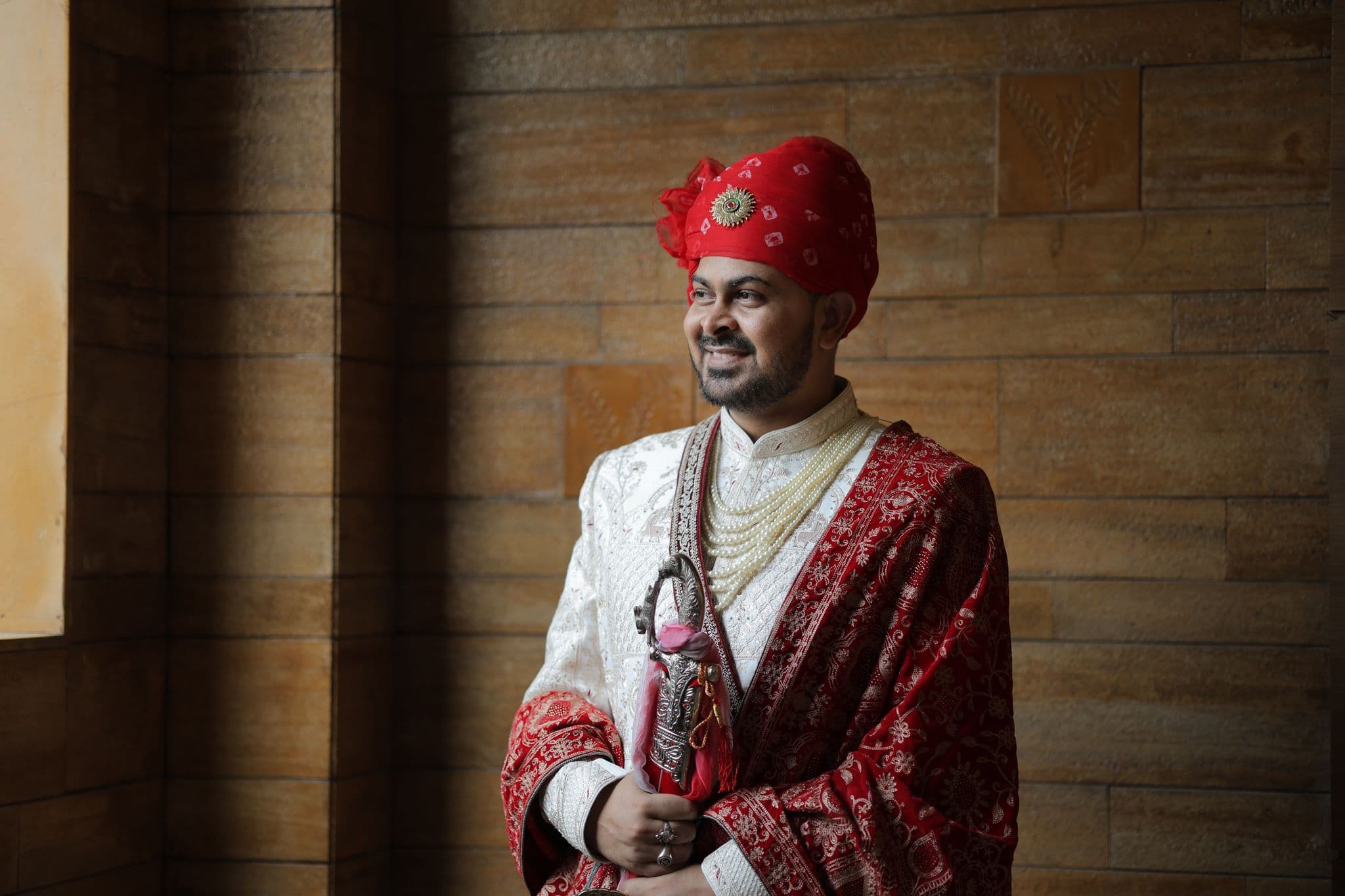 A groom in a red turban and maroon embroidered shawl