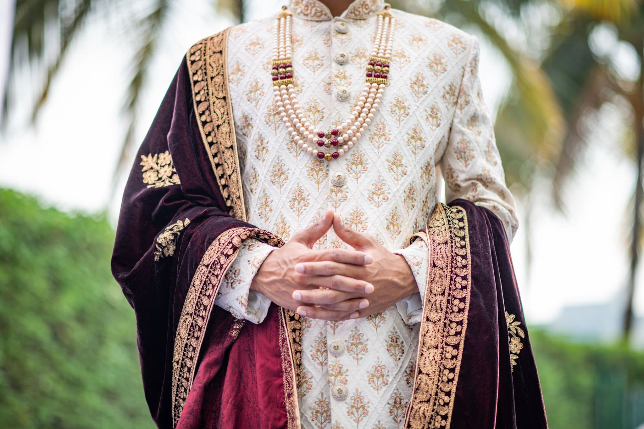 Close detail of an embroidered ivory sherwani with a maroon velvet stole and pearls